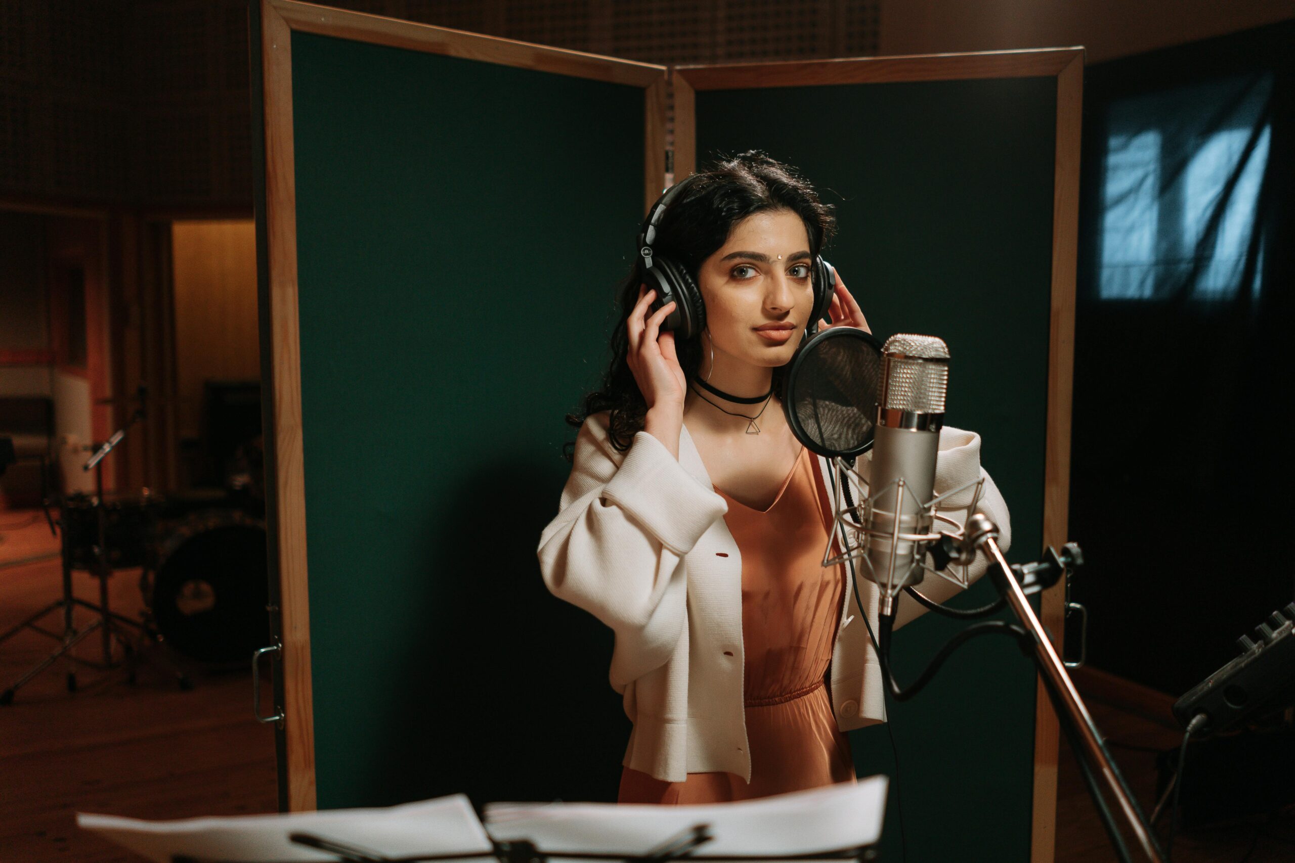 A female musician recording vocals in a professional music studio.